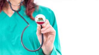 An unseen female doctor holds up a stethoscope bearing the California state flag. | Allexxandar | Dreamstime.com