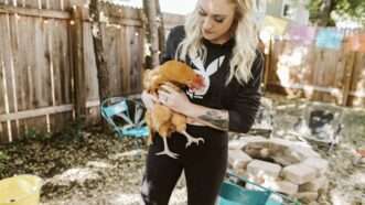 Liz Wolfe stands in a backyard, holding a chicken | Liz Wolfe