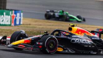Side view of a Red Bull Racing F1 car going through a turn, with a green Stake F1 car in the background | Jay Hirano/AFLO/Newscom