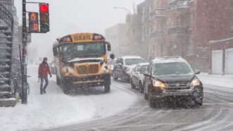 A Montreal school bus sits at a red light in snowy conditions, with cars on one side. | Marc Bruxelle | Dreamstime.com