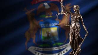 Michigan US state flag with statue of lady justice and judicial scales in dark room. | Mehaniq/Newscom