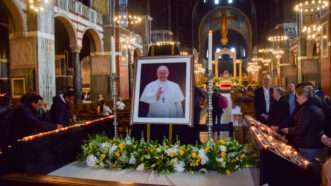 Image of Pope Francis in a church, surrounded by flowers and candles | Vuk Valcic