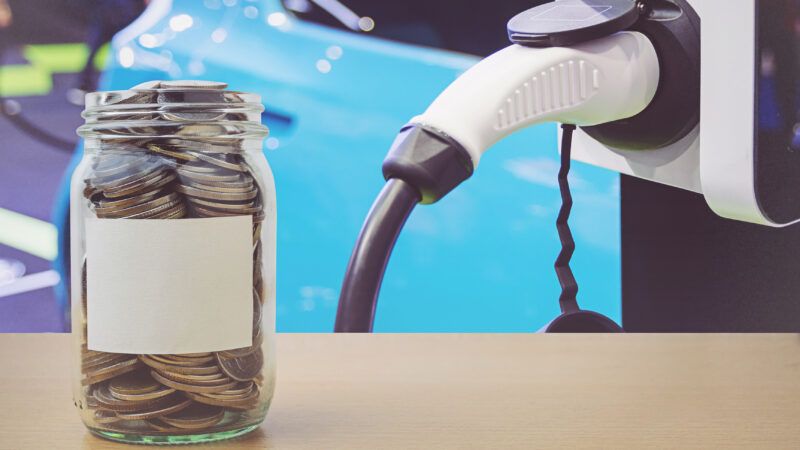 A jar full of coins alongside an electric vehicle and charger. | Pichai Pipatkuldilok | Dreamstime.com